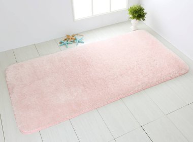 Beyaz ahşap zeminde pembe banyo halısı.