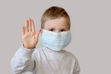 Cerrahi maskeli çocuk elleriyle durduğunu gösteriyor..