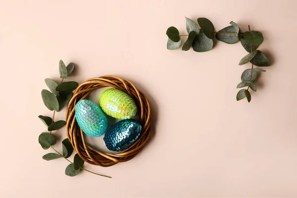 Uova di Pasqua lucide colorate nel nido di rattan. Ramo di eucalipto naturale sul retro. Copia lo spazio per testo o design . — Foto Stock