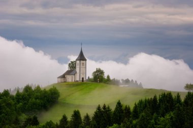 İlkbaharda bir yamaçtaki Jamnik kilisesi, Slovenya, Avrupa 'da günbatımında sisli hava. Bahar yağmurundan kısa bir süre sonra dağ manzarası. Slovenya Alpleri.