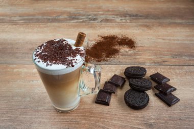 Kahverengi bisküviler ve kahverengi tahta üzerinde çikolata parçalarıyla cam bardakta kapuçino..