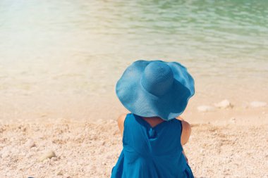 Yaz elbisesi ve şapkalı genç kadın kumun üzerinde duruyor ve Yunanistan 'ın Porto Vromi limanına bakıyor.