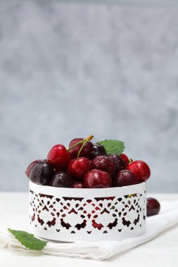 Taze kiraz kasesi. Beyaz ahşap masada su damlalarında yapraklar var..