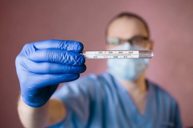 Adam termometreyi eline tut. Cerrahi maskeli doktor ısıyı kontrol ediyor..