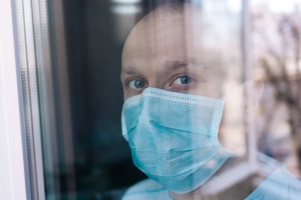 Portrait of a man in surgical mask. Stop epidemic. Epidemic infection. Stop coronavirus. Quarantine. Stay home. Man look through the window