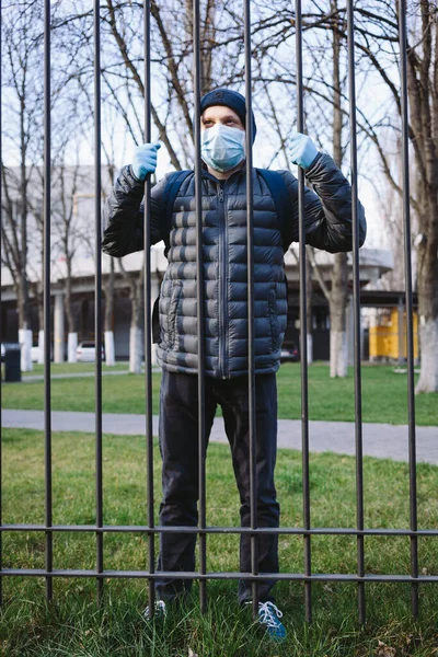 Portrait of young man in surgical mask and gloves near the grid. Pandemic coronavirus 2020. Quarantine.