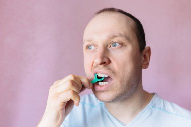 Bir adam dişlerini diş ipiyle fırçalar. Sağlık hizmetleri sabahı. Güne doğru başla. Günaydın.. 