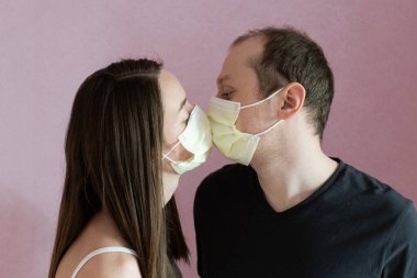 Erkek arkadaşı sarı koruyucu maskeli kız arkadaşını öpüyor. Pembe arka plan. 2020 pandemik koronavirüs. Karantinaya alın. Virüs konsepti. Salgın hastalık. 