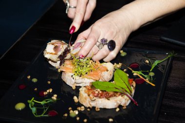 Bir kadının elleri somon, kimyon ve yeşil şeylerle bruschetta kesiyor. Kırmızı balık ve sebzeli sandviç.. 