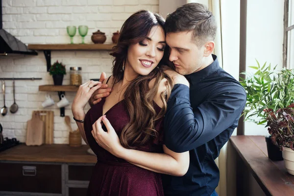 A lovely couple are standing in the kitchen with closed eyes. A smiling woman in dress with a yellow tulips in her hand. Harmonious family. Romantic love story. Happiness.