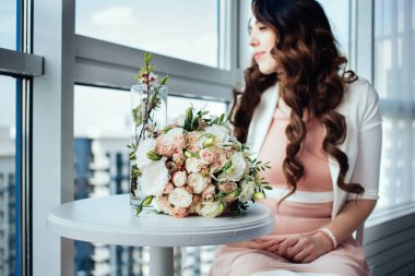 Güzel elbiseli bir kız kafede oturuyor ve pencereye bakıyor. Masada ot buketi var. Güneşli bir yaz gününde, uzun siyah kıvırcık saçlı, lüks ve zarif bir bayan..