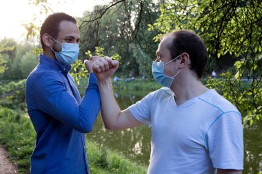 Orta Doğulu ve parktaki koruyucu maskeli beyaz bir genci selamlıyorum. Selamlar, merhaba. Sosyal mesafe. 2020 pandemik koronavirüs. Karantina Virüsü Konsepti