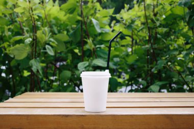 Parkta yeşil arkaplan ve siyah kamışlı beyaz bir kağıt bardak. Kahve ya da çay. Çevre. Ayrıl. Yaz günü