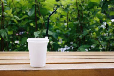 Parkta yeşil arkaplan ve siyah kamışlı beyaz bir kağıt bardak. Kahve ya da çay. Çevre. Ayrıl. Yaz günü