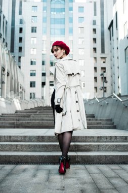 Şehrin iş merkezinin yanındaki merdivenlerde yürüyen açık renk pelerinli, siyah elbiseli, kırmızı bereli genç zarif bir kızın arkası. Bahar günü. Yüksek topuklu iş kadını arkasına bakıyor. Yaşam biçimi. 