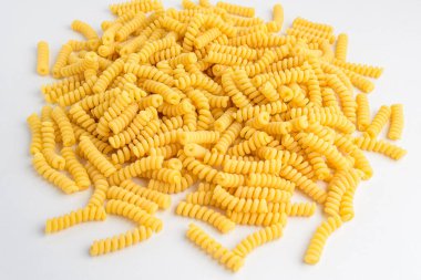 Kurumuş fusilli İtalyan makarnası, beyaz bir masada rastgele sergileniyor, pişirilmeye hazır, beyaz arka planda izole edilmiş, sağlıklı yiyeceklerin yan görüntüsü. 