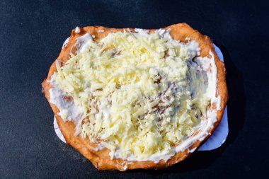 Bir langoya yakın, tipik bir Macar yemek spesiyali, ekşi krema ve peynirli, siyah bir masada beyaz bir tabakta, güneşte kızartılmış hamur, bir gıda pazarında. 