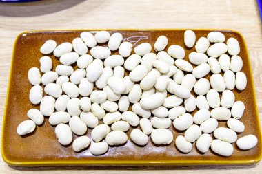 Masadaki kahverengi bir tabakta pişmeye hazır bir sürü beyaz fasulye, bir sokak yiyecek pazarında, yan görüşte veya düz bir resimde sağlıklı yiyecekler sergileniyor.