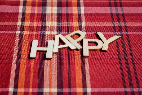 Happy word written with wooden letters on red textile material with colored stripes, top view, flat lay