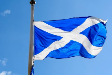 İskoçya bayrağı (Saltire veya Saint Andrew Haçı) güneşli bir günde açık mavi gökyüzüne doğru esen rüzgarda