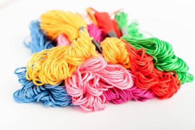 Birçok canlı renkli nakış iplikleri beyaz bir masada izole edilmiş bir daire içinde gösterilir, kırmızı, pembe, sarı, mavi, siyah ve yeşil tekstil materyalleri