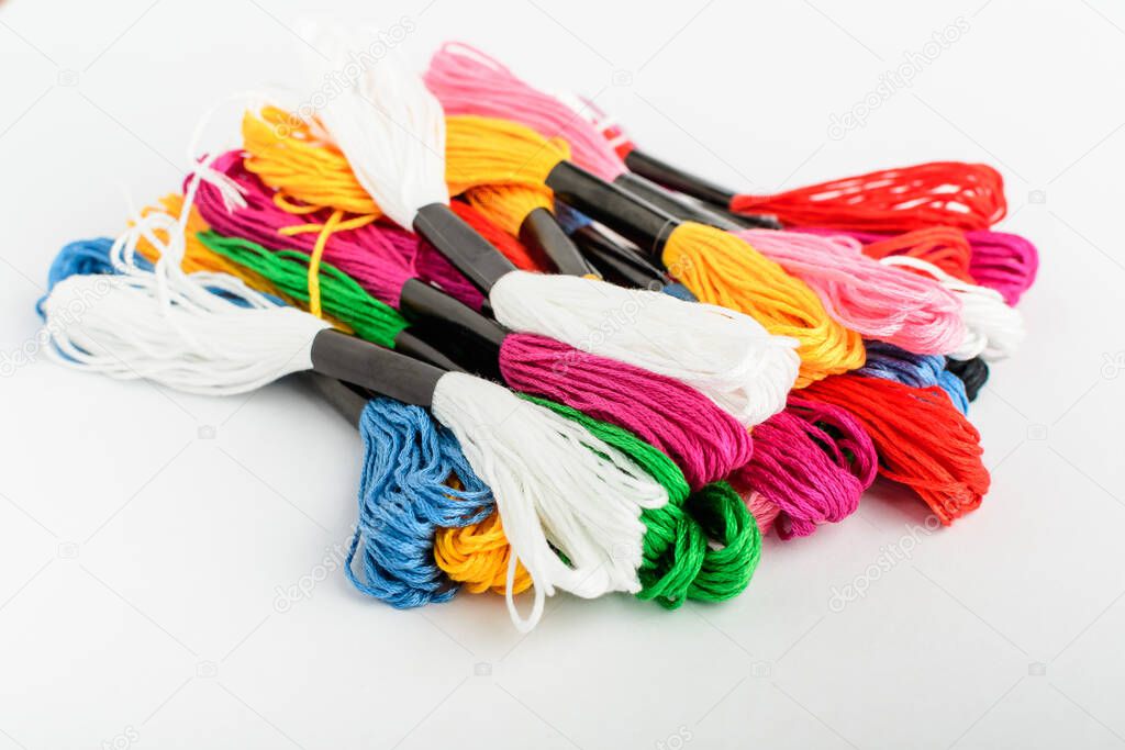 Many mixed colored sewing threads for embroidery on a white table, side view of red, pink, yellow, blue, black and green textile materials