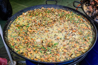 Bir sokak yemeği festivalinde domates ve krema soslu büyük bir grup pişirilmiş midye, deniz ürünleri yemeye hazır, güzel turuncu tek renkli arka plan.