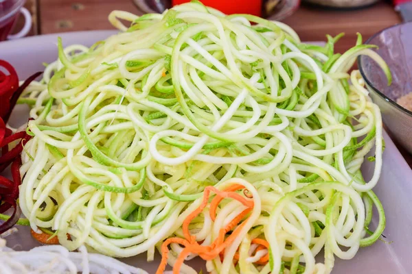 Fresh cut white and green organic zucchini cut as spaghetti, ready to be cooked on a kitchen table, side view of healthy vegan food photographed with soft focus