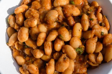 Domates sosu ve acı baharatlarla pişirilmiş büyük bir porsiyon beyaz fasulyeyi bir sokak gıda pazarında sergilenirken, sağlıklı vejetaryen yemekleri yumuşak odaklanarak fotoğraflandı.