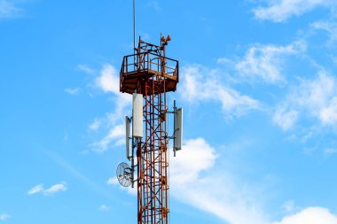 Telekomünikasyon antenleri kırmızı ve beyaz bir telekomünikasyon kulesinde ve arka planda açık mavi gökyüzü