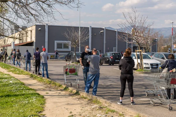 Tuscany, İtalya - 03 / 21 / 2020: Coronavirus COVID-19 salgını, alışveriş arabalarıyla bir süpermarkete girmek için kuyruk oluşmuş uzun insanlar, salgın zamanlarında yiyecek stokları için acele ediyorlar