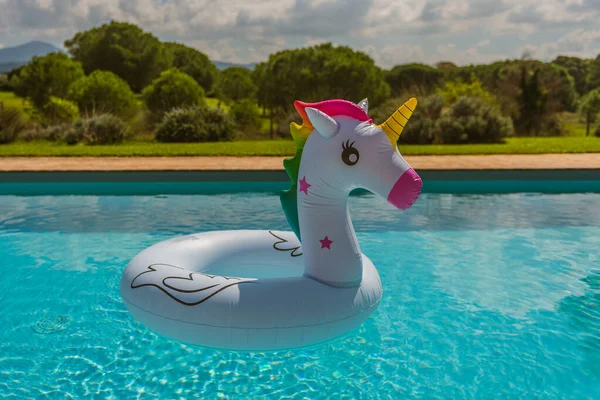inflatable in the shape of a unicorn in the pool, summer in the Italian countryside, surreal and funny