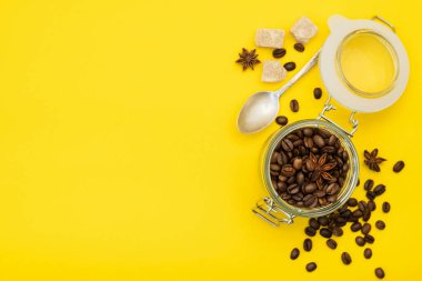 Bardakta kahve çekirdeği, anason, kamış şekeri ve parlak sarı bir arka planda kaşık. Boşluğu kopyala.