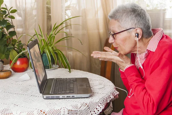 Бабушка с помощью ноутбука, камеры и наушников для удаленных соединений — стоковое фото