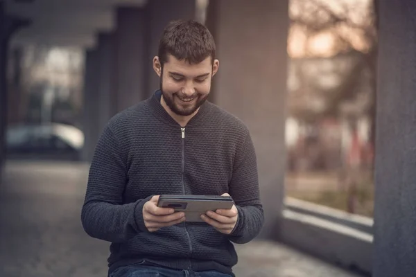 Pohledný mladý muž messaging kamaráda na jeho tablet v městské oblasti — Stock fotografie