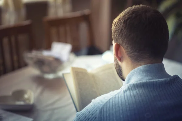 Jeune homme lisant un livre, assis sur une chaise dans son salon — Photo