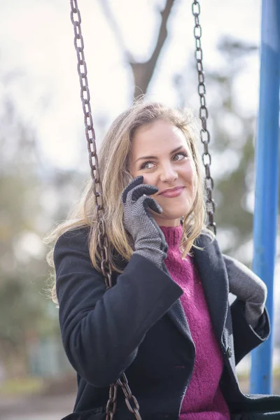 Douce jeune femme ayant une belle conversation tout en se balançant dans un parc — Photo