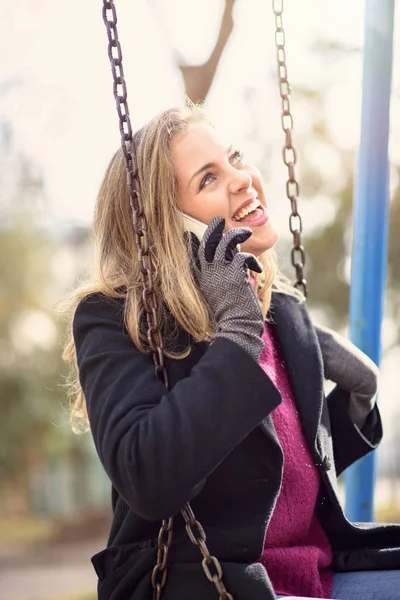 Douce jeune femme ayant une belle conversation tout en se balançant dans un parc — Photo