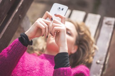 Güneşli bir günde bir parkta cep telefonunu kullanan ücretsiz neşeli kadın