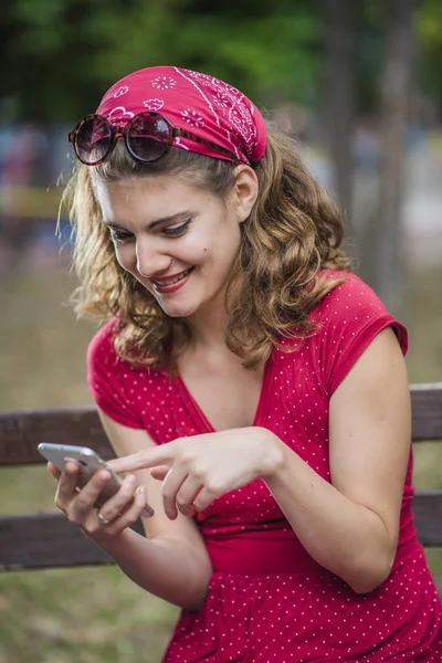 Κομψό κορίτσι σε ένα κόκκινο φόρεμα που ελέγχει το τηλέφωνό της για τα μηνύματα — Φωτογραφία Αρχείου