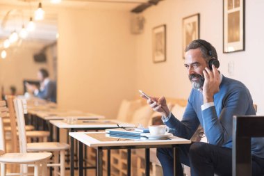 Kıdemli yaşlı adam büyük kulaklıklarla en sevdiği müziği dinliyor, müziğin zengin sesinin tadını çıkarıyor, bir kafede oturuyor.