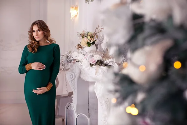 クリスマス インテリア クリスマス ツリー近くの緑色のドレスの美しいブルネット妊婦 — ストック写真