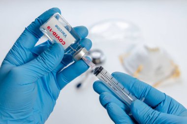 Doktor ya da hemşire elinde kovid 19 aşı şişesi ve şırınga tutan mavi eldivenleri teslim etti. tıp ve uyuşturucu kavramı.