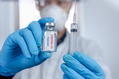 Sağlık tedavisi konsepti. Bir doktor elinde mavi tıbbi eldivenlerle aşı tutuyor. Coronavirus krizi sırasında, Covid 19 virüsü, aşı şişesi