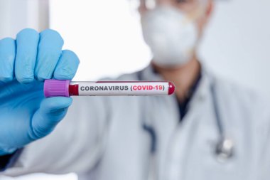Coronavirus (COVID-19) için hastaların kan örneklerini test eden doktor, üzerinde Amerika bayrağı bulunan bir kan örneği içeren bir test tüpü tutuyor..