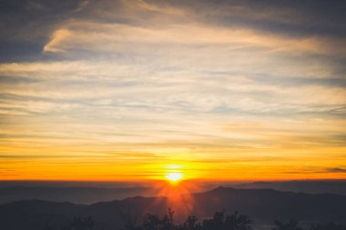 Güneşin doğuşu dağın tepesinde bulutlarla aydınlanan gökyüzü