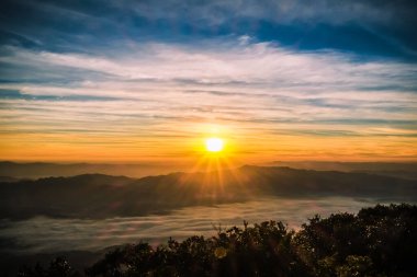 Güneşin doğuşu dağın tepesinde bulutlarla aydınlanan gökyüzü