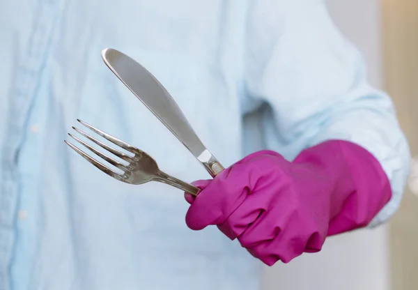 Garfo e faca na mão em uma luva roxa doméstica, desinfecção e esterilização — Fotografia de Stock