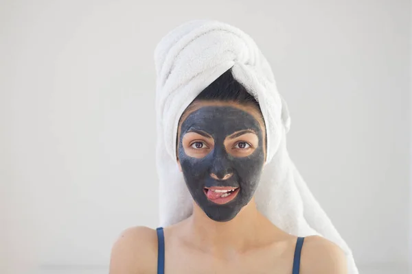 funny girl shows tongue, on face a black cleansing mask