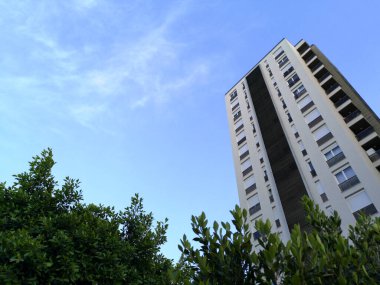 Mavi gökyüzü arka planına sahip, modern beyaz bir apartman manzarası.